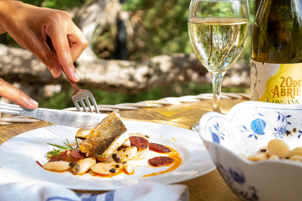 Tischsituation mit angerichtetem Bohnensalat und Fisch auf Teller, Weinflasche und Glas im Hintergrund